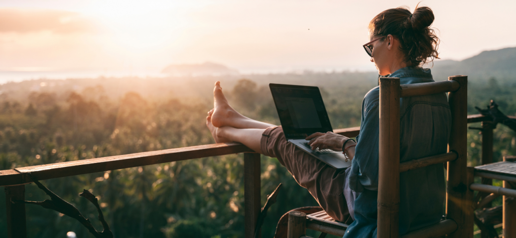 A woman works remotely on a laptop with a scenic view.