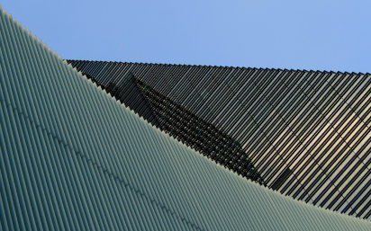 Abstract close-up of curved textured surfaces with diagonal striped patterns against a blue sky.