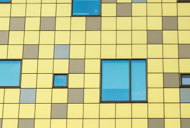A building façade with a yellow grid pattern interspersed with blue and gray windows of varying sizes.