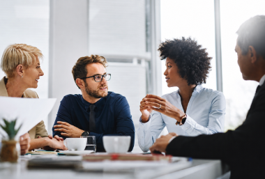 Four coworkers engaged in a collaborative discussion around a meeting table in an office.