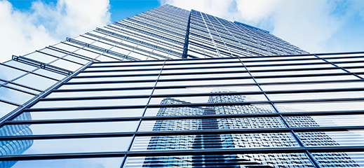 Low-angle view looking up at the glass facade of a modern corporate skyscraper against a blue sky.