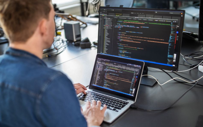 Software developer working on code across multiple computer screens in an office.