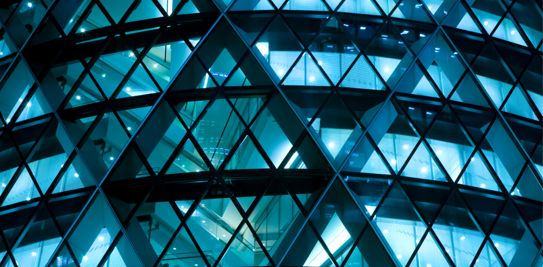 Modern glass building facade with illuminated geometric triangular windows at night.