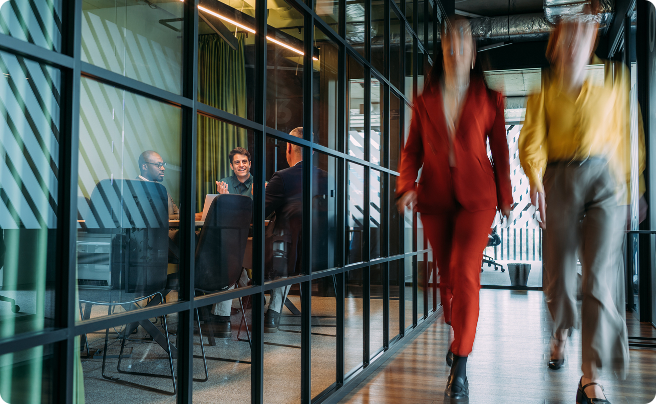 Colleagues walking through a modern office with glass meeting rooms.