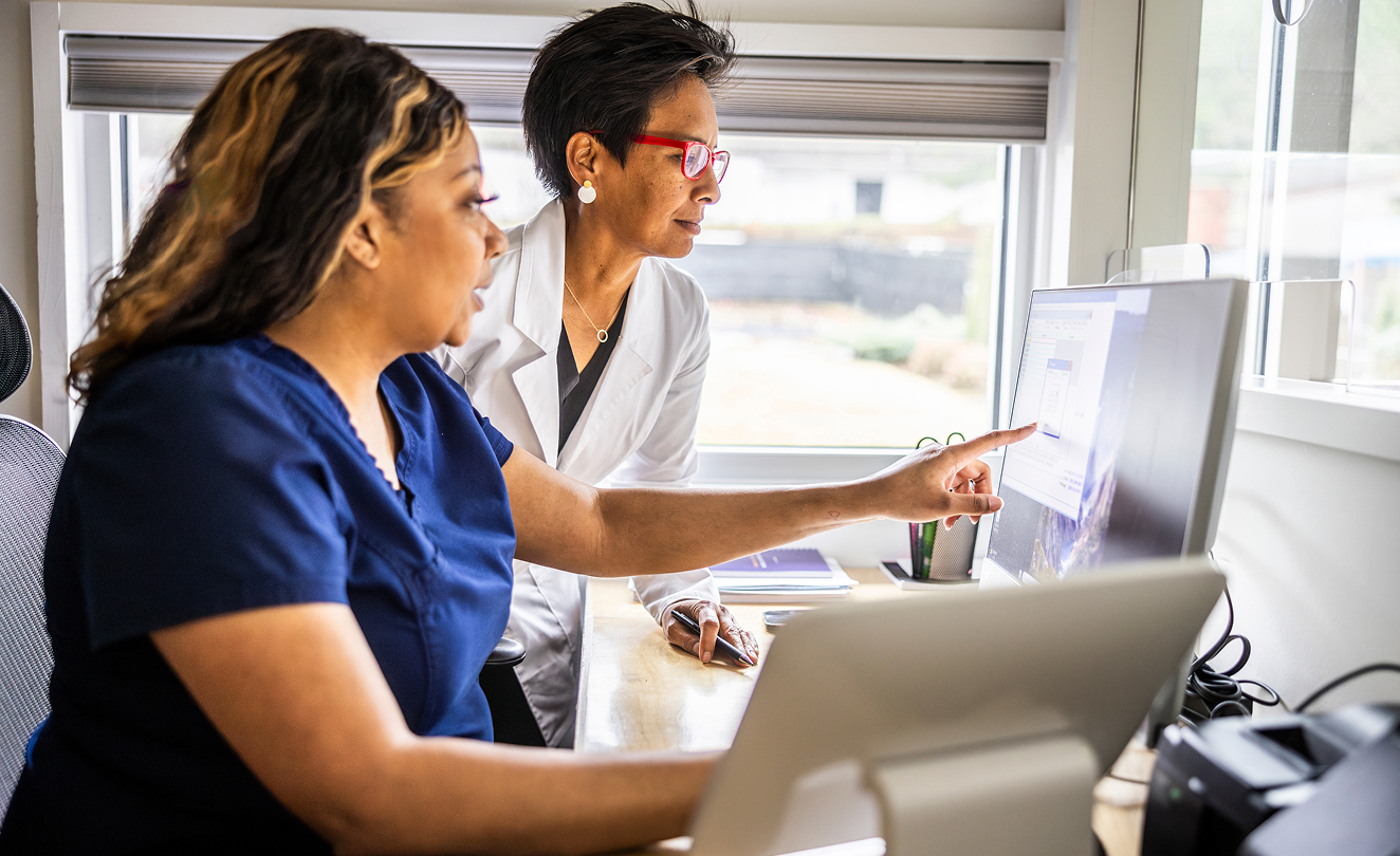 Healthcare professionals reviewing medical information on a computer in a clinical setting.