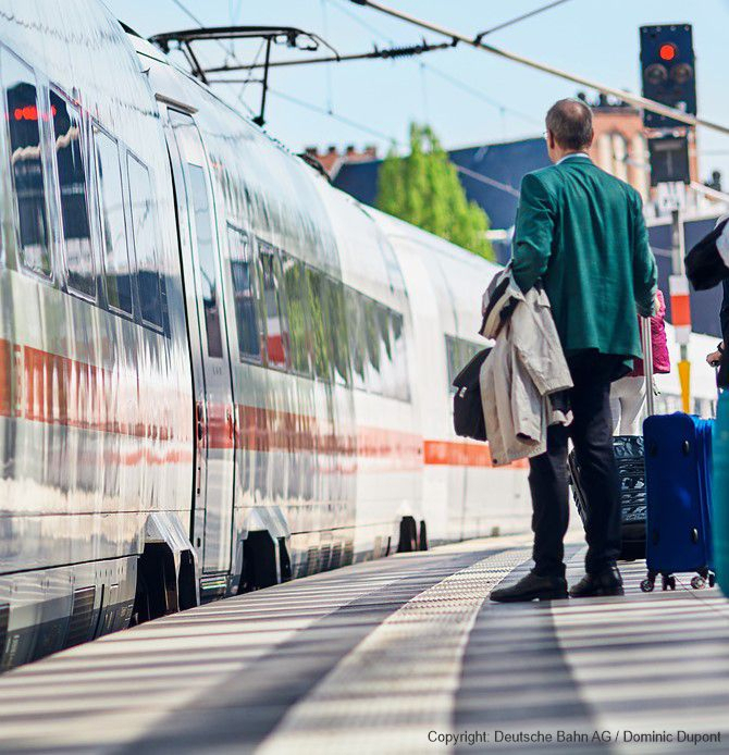Person with luggage standing on a train platform beside a white and grey train