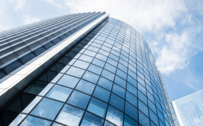 A low-angle view of a modern glass skyscraper with a curved facade reflecting the sky and clouds