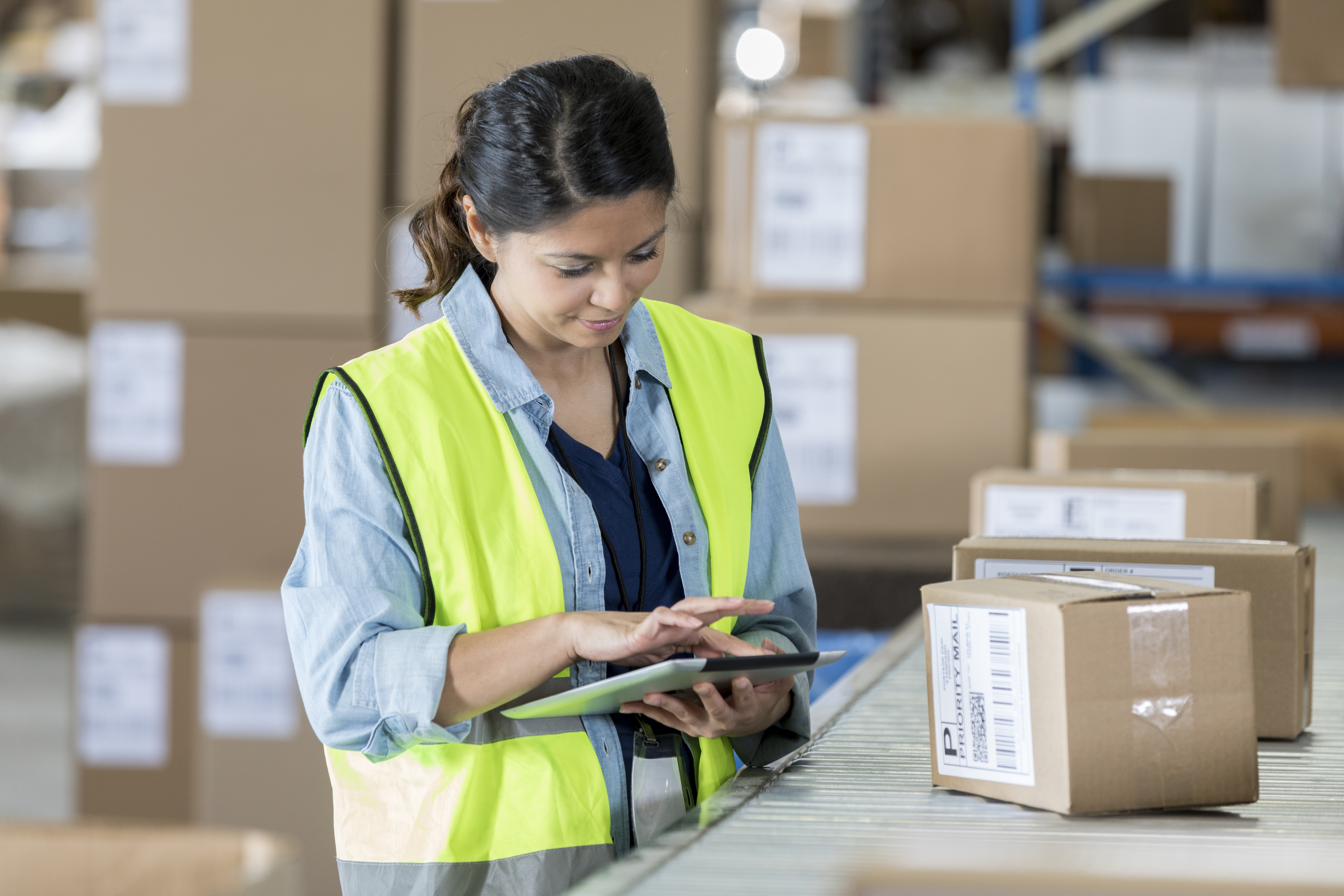 Confident female warehouse manager using a tablet to track packages on a distribution conveyor line.