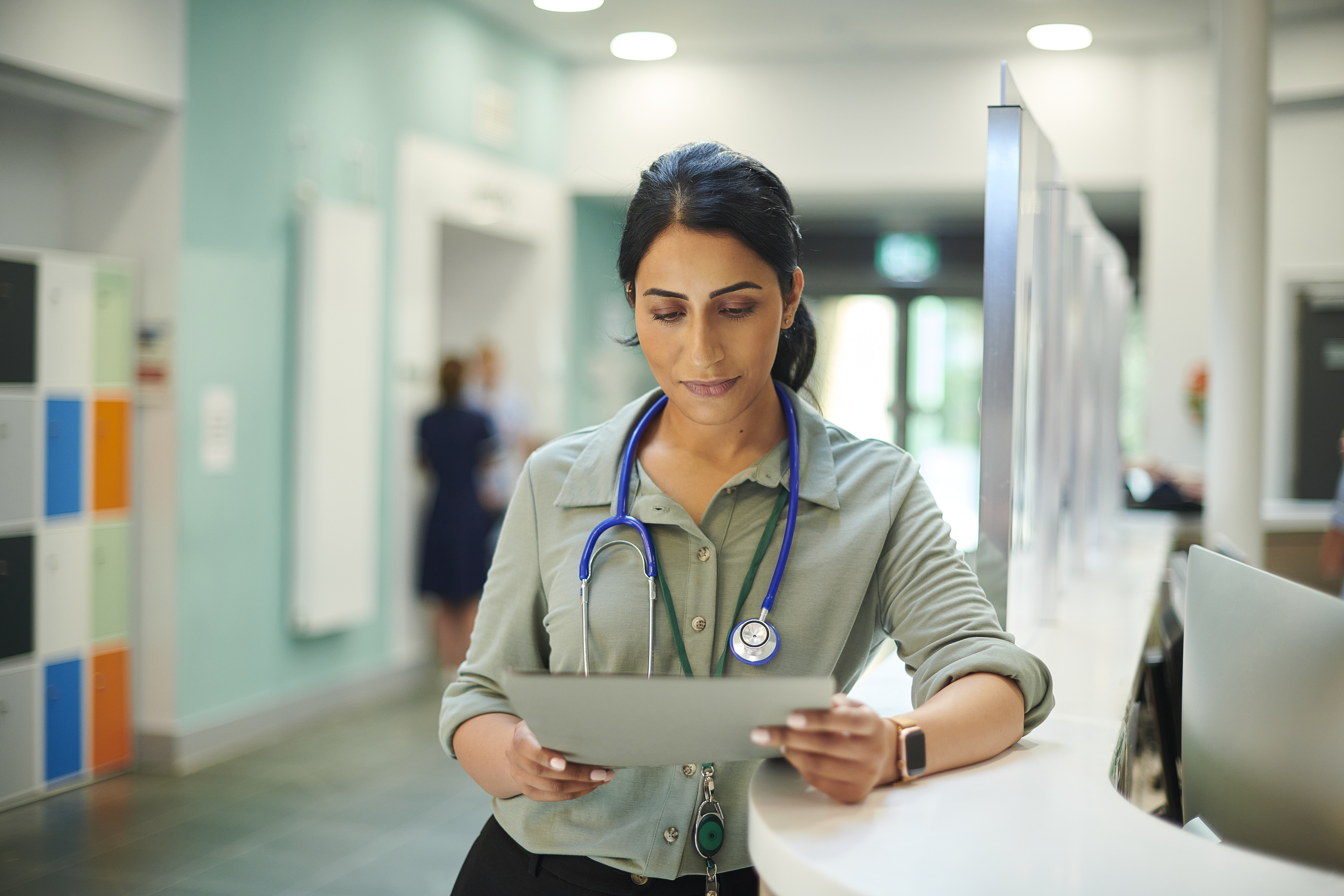 Healthcare professional reviewing patient information on a tablet at a hospital reception desk.