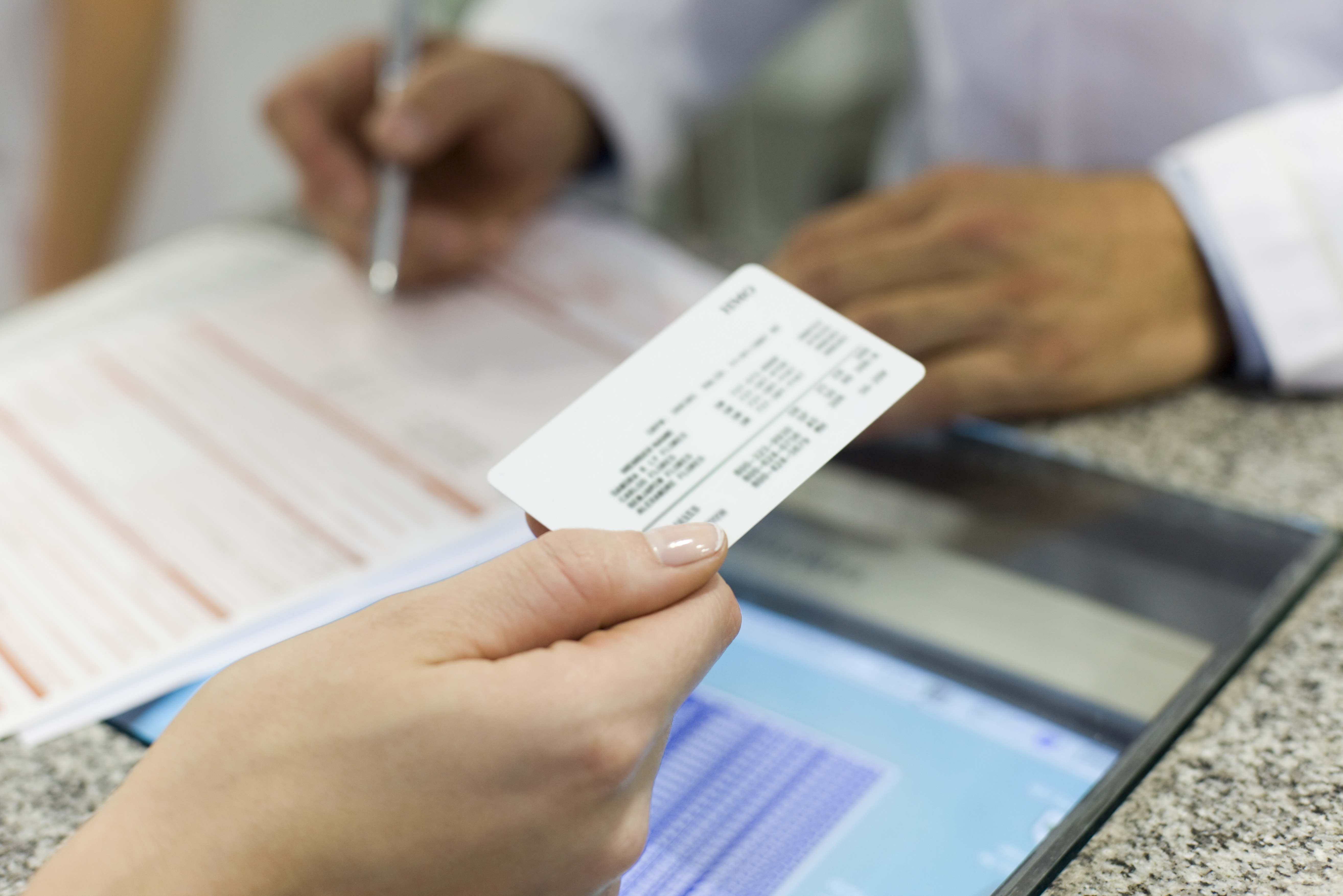 Close-up of a customer presenting a health insurance card during a medical service interaction.