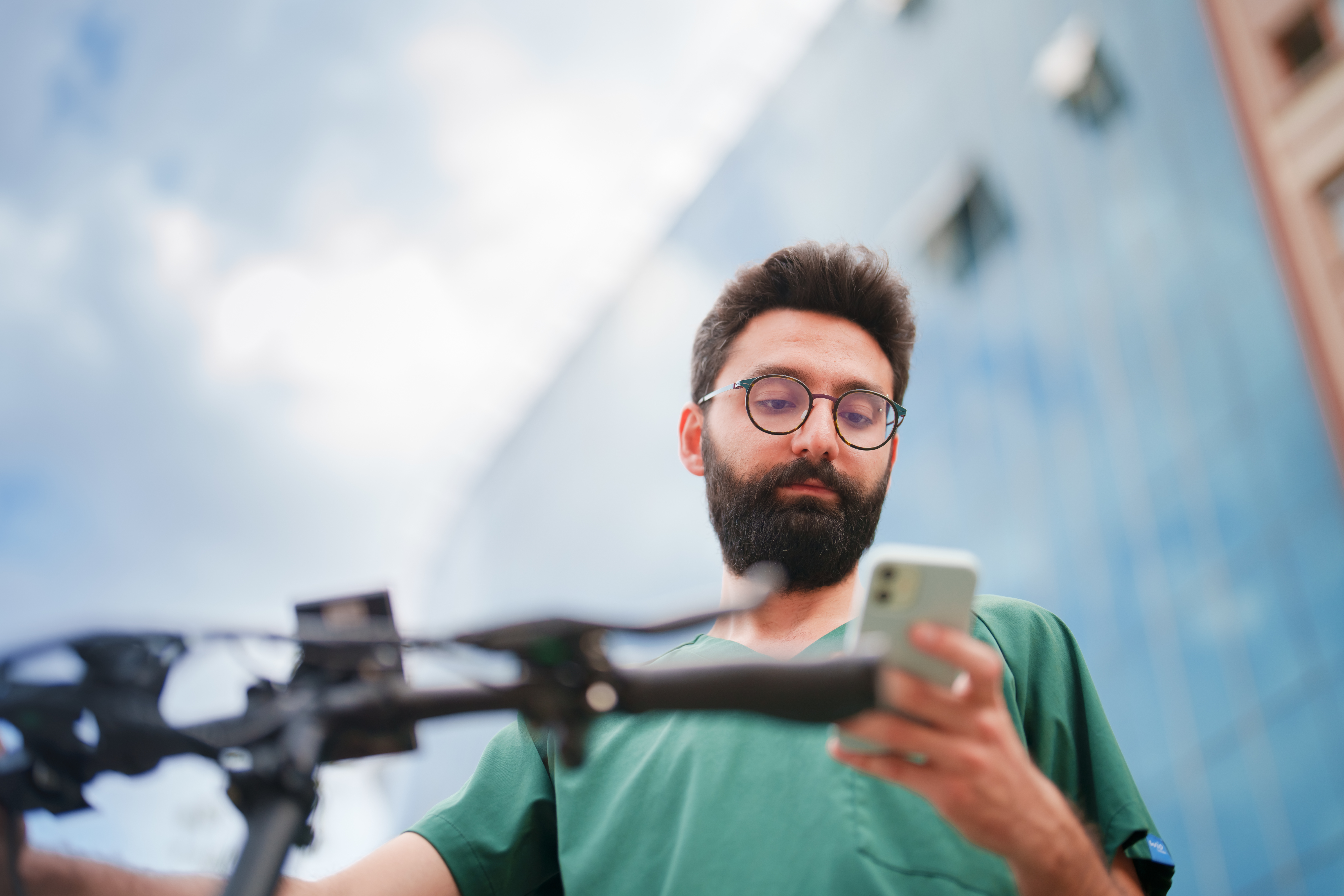 Bearded man checking his phone while standing beside an electric bike outdoors.