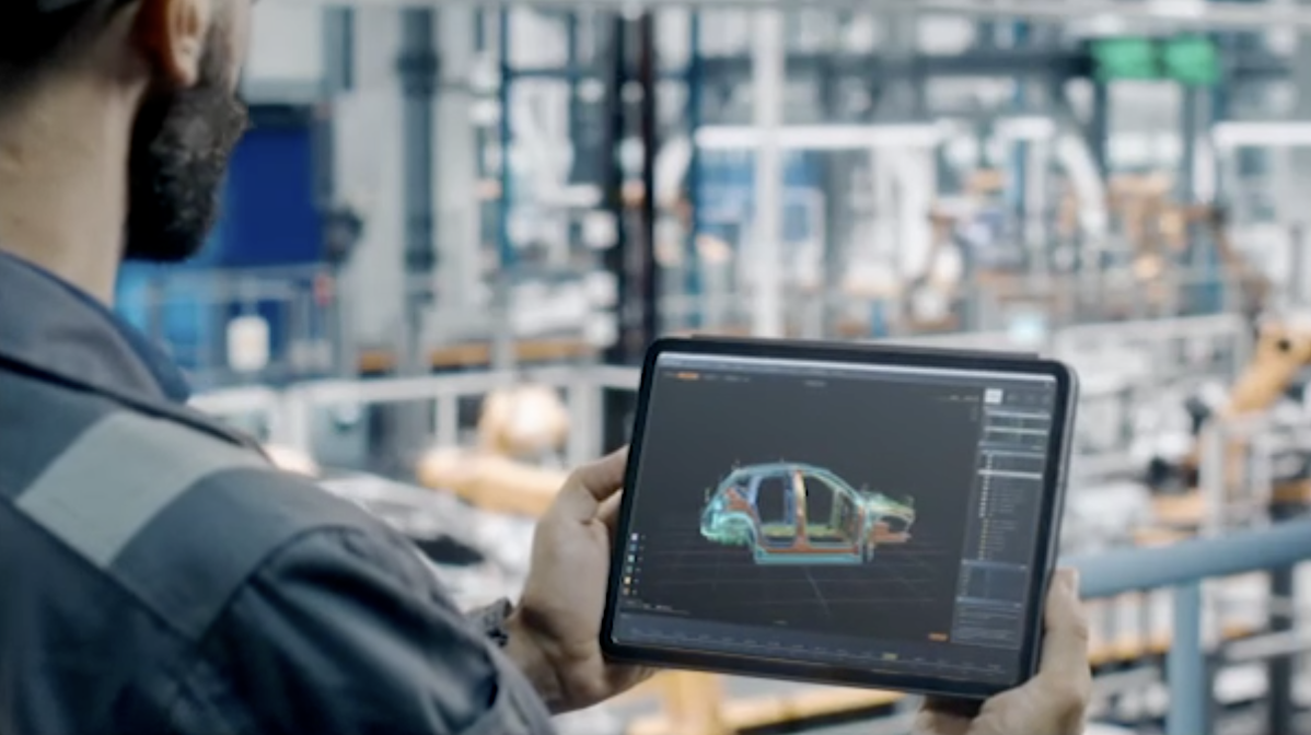 Worker in a manufacturing facility looking at a 3d rendering of a car on a tablet