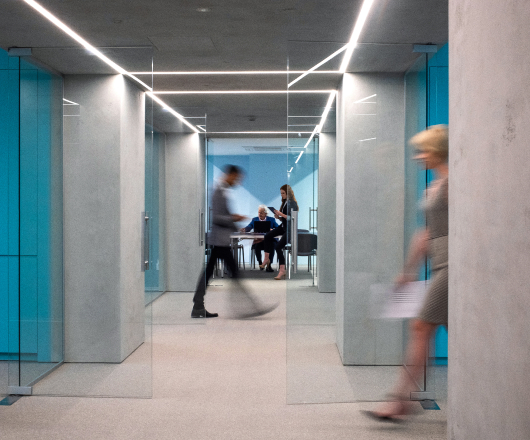 Modern office hallway with people in motion and a meeting room visible in the background