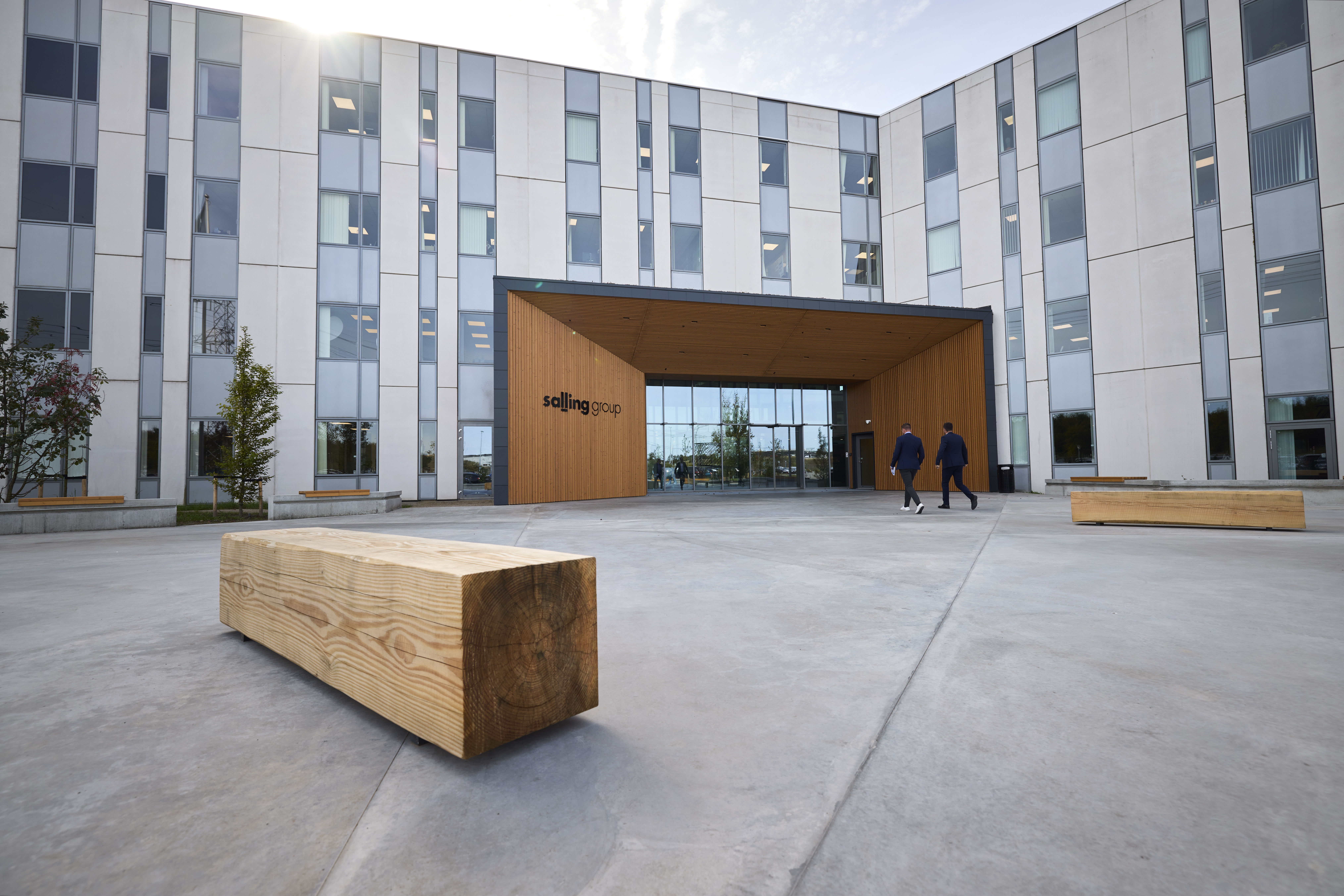 Modern office building with a wooden entrance labeled “Selling Group” and two people walking toward it.