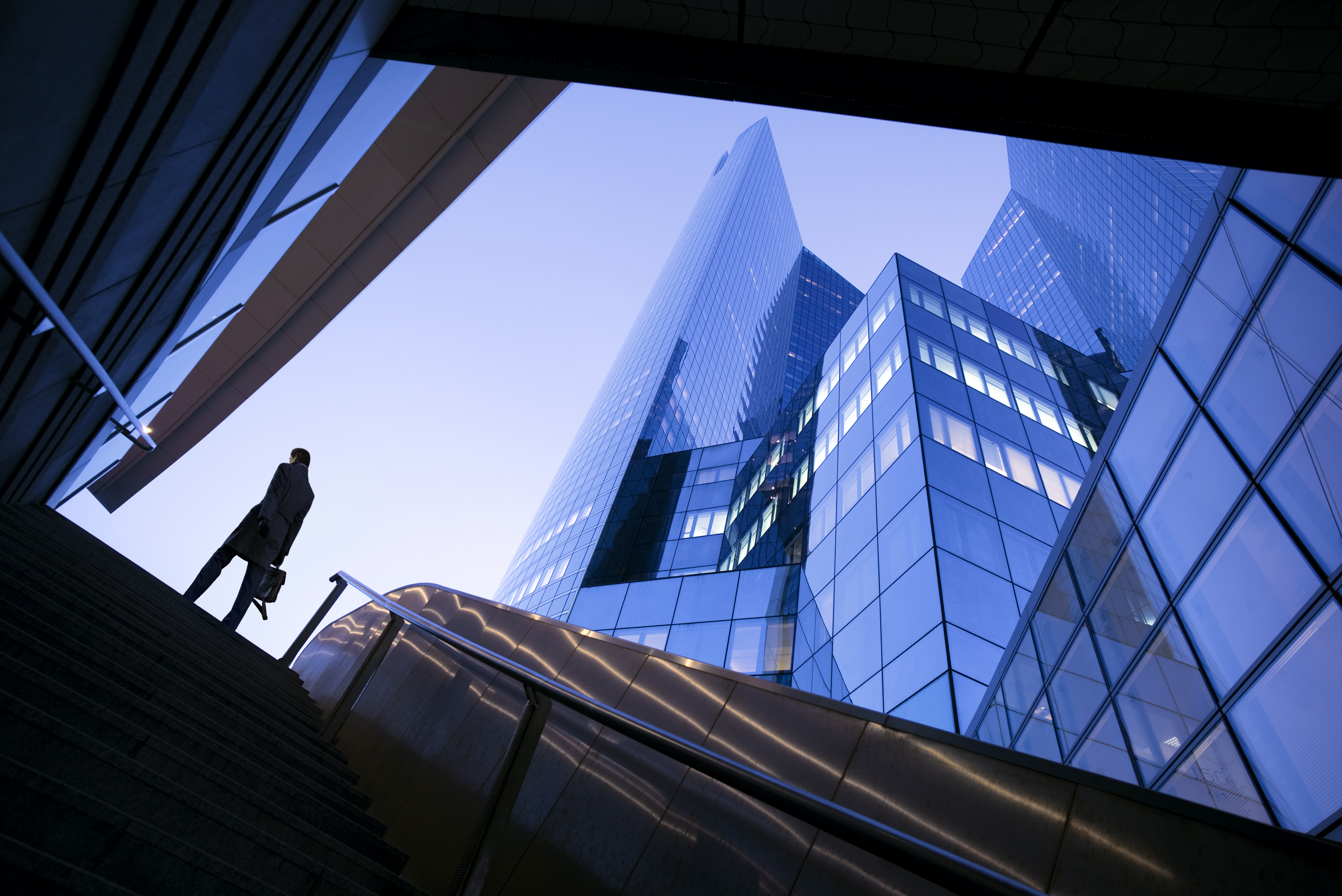 Silhouette of a person beside a modern glass skyscraper viewed from below.