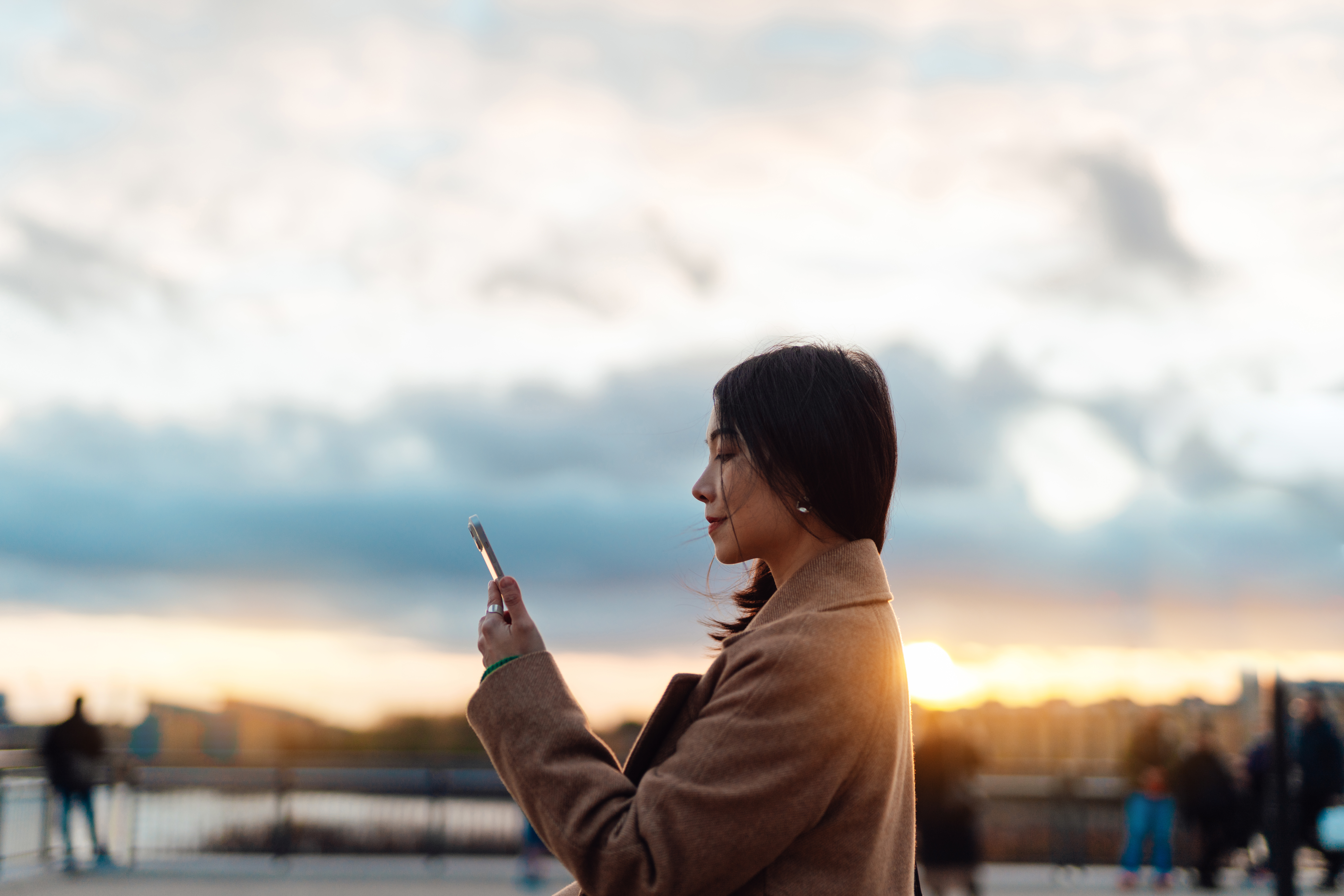 Young Asian woman using a smartphone outdoors at sunset.
