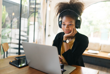 Person wearing headphones working on a laptop at a wooden table